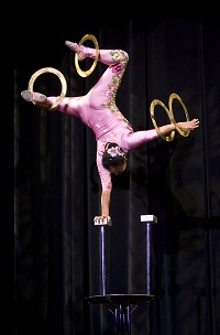 Photo of an acrobat balancing on one hand and spinning rings on her feet and other hand